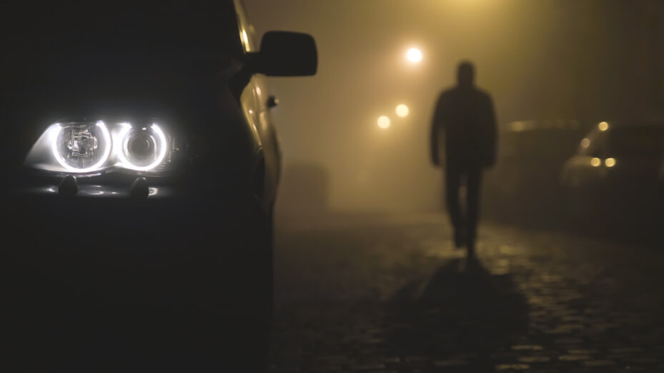 The,Car,Headlight,With,A,Walking,Man,On,The,Background