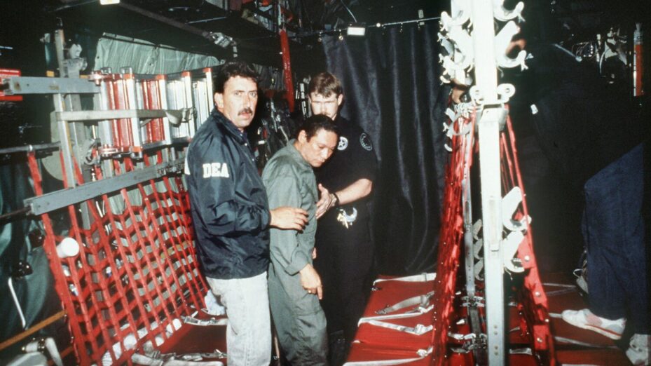 In this photo released 04 January 1990 by the Defense Department, Panamian General Manuel Noriega (C) is brought on board a US military plane 3 January 1990 for a flight to Miami after his arrest. (Photo by AFP)